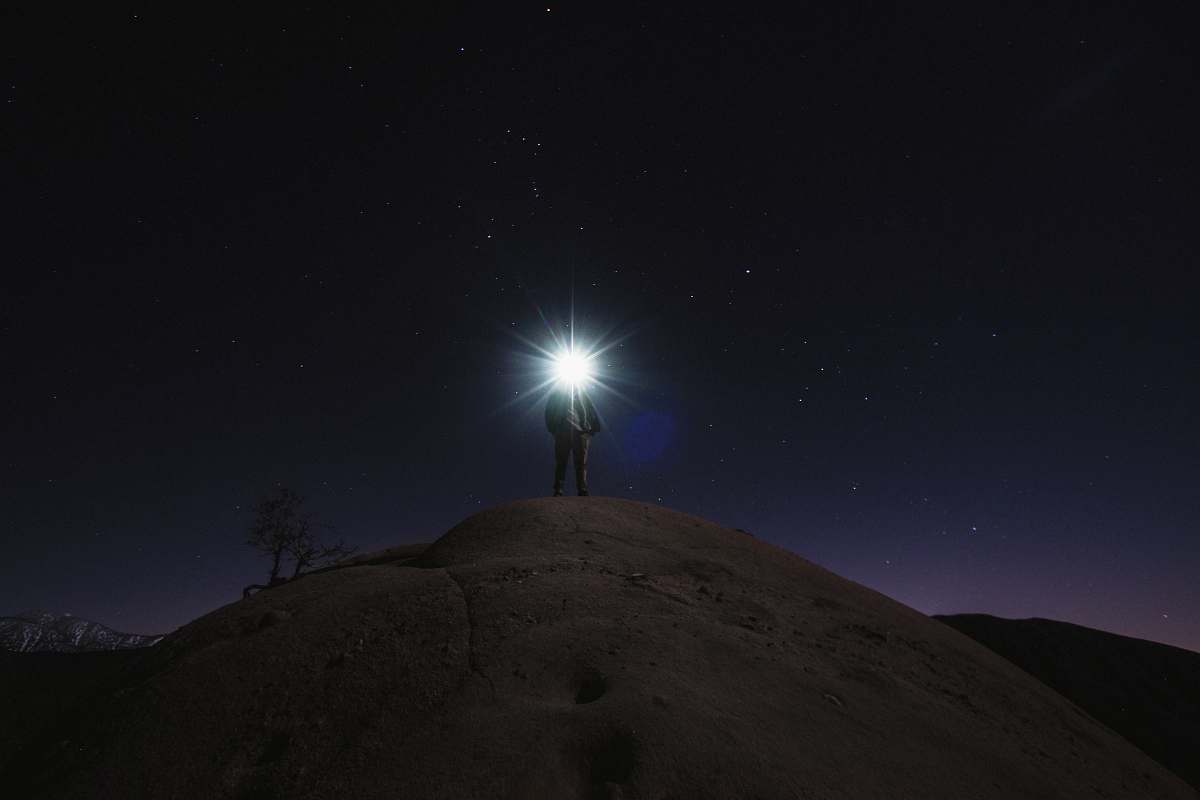 night sky man standing on mountain white holding flashlight stars